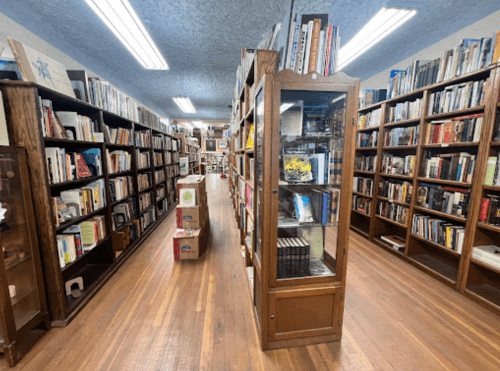 A cozy bookstore aisle lined with wooden shelves filled with books, featuring a glass display case in the center.